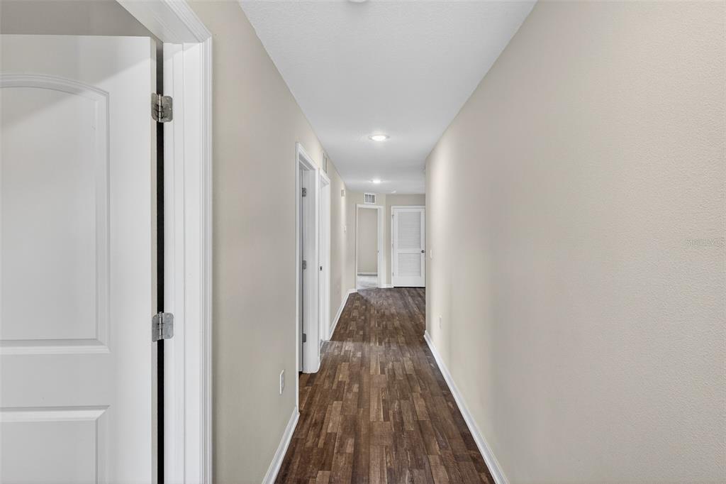 A hallway with light-colored walls and wood-look flooring leads to several closed white doors — 842 GILA WAY, KISSIMMEE, FL