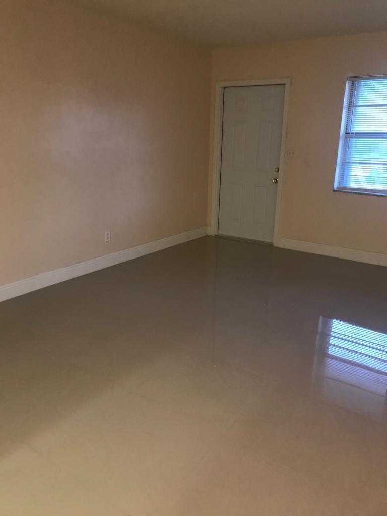An empty room with beige walls, white trim, a white door, and glossy tile flooring — DEERFIELD BEACH, FL