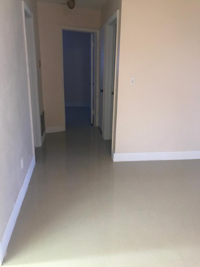 A hallway with light-colored walls and tile flooring leads to an open doorway — DEERFIELD BEACH, FL