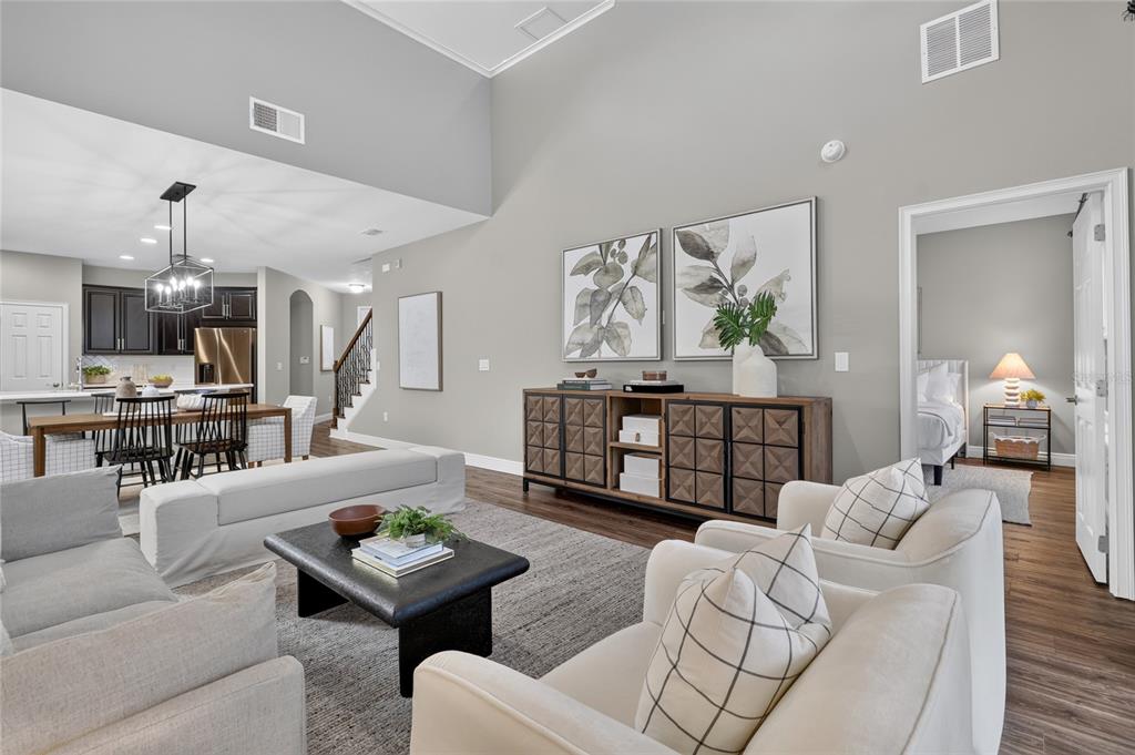 An open-concept living room features a vaulted ceiling, neutral furniture, and a wooden media console — 517 RED ROSE LANE, SANFORD, FL