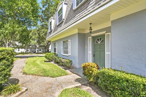 A gray house exterior features a green front door, a walkway, and manicured landscaping — 1717 BELLEAIR FOREST DRIVE UNIT A, CLEARWATER, FL