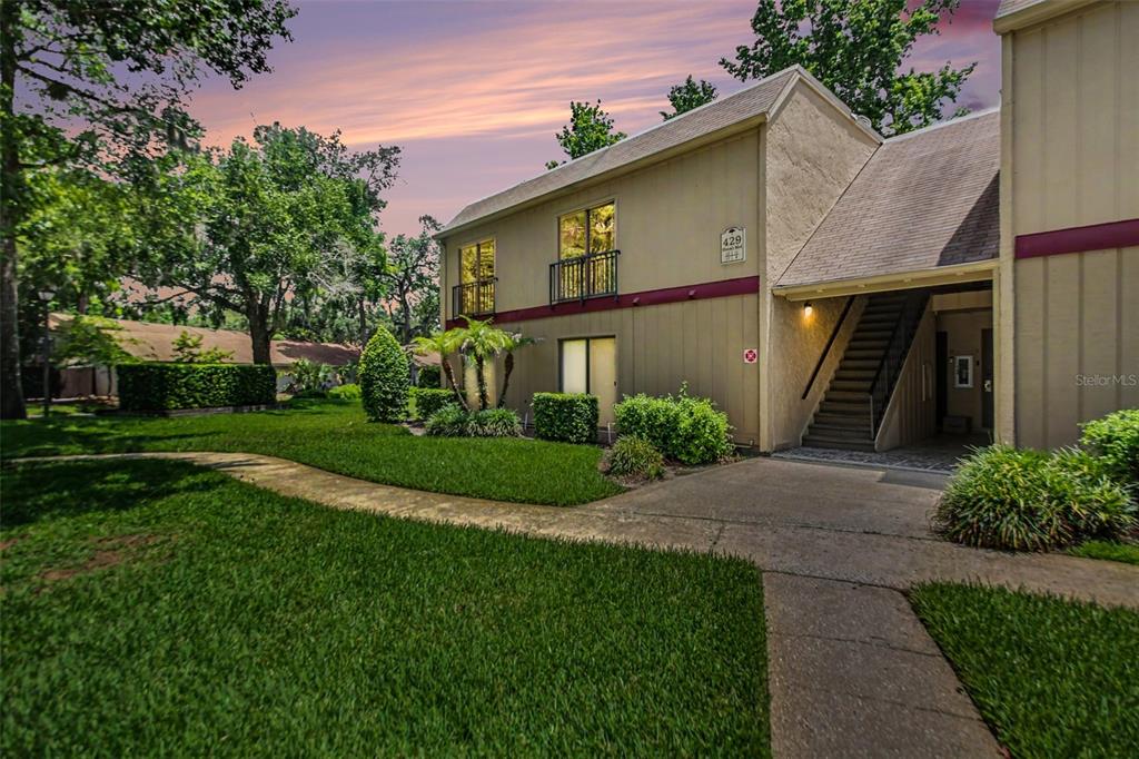 A two-story tan apartment building features a concrete walkway, exterior stairs, and landscaped green space — 429 SHEOAH BOULEVARD UNIT 9, WINTER SPRINGS, FL