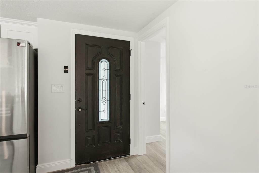 A dark brown front door with a glass insert sits next to a stainless refrigerator — 4930 POMPANO DRIVE, NEW PORT RICHEY, FL