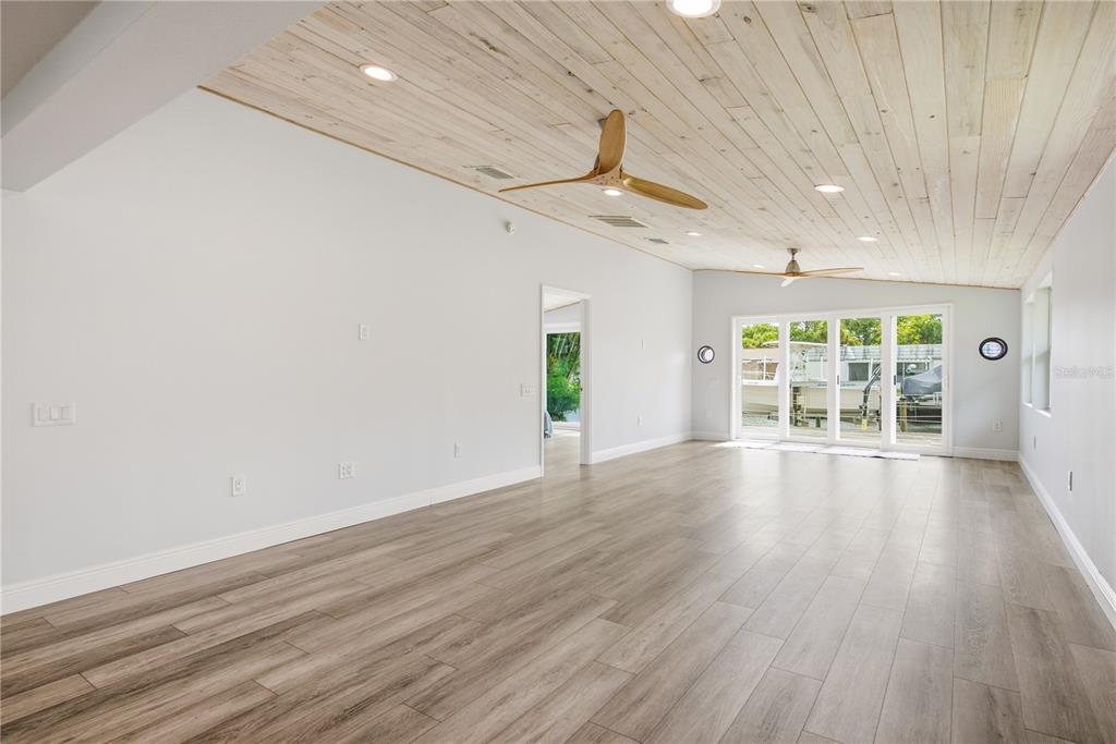 A spacious room features light wood plank flooring, a vaulted wood-paneled ceiling, and sliding glass doors — 4930 POMPANO DRIVE, NEW PORT RICHEY, FL
