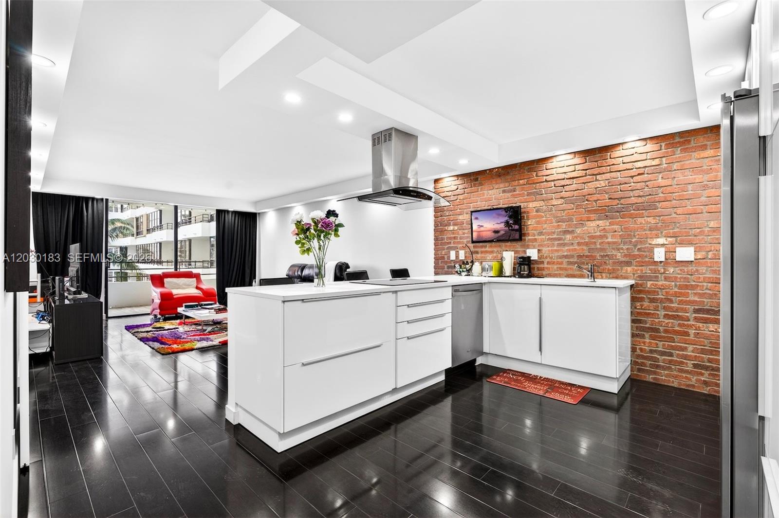 A modern kitchen with white cabinets and a brick wall overlooks a living area — 500 Three Islands Blvd # 201, Hallandale Beach FL 33009, HALLANDALE BEACH, FL
