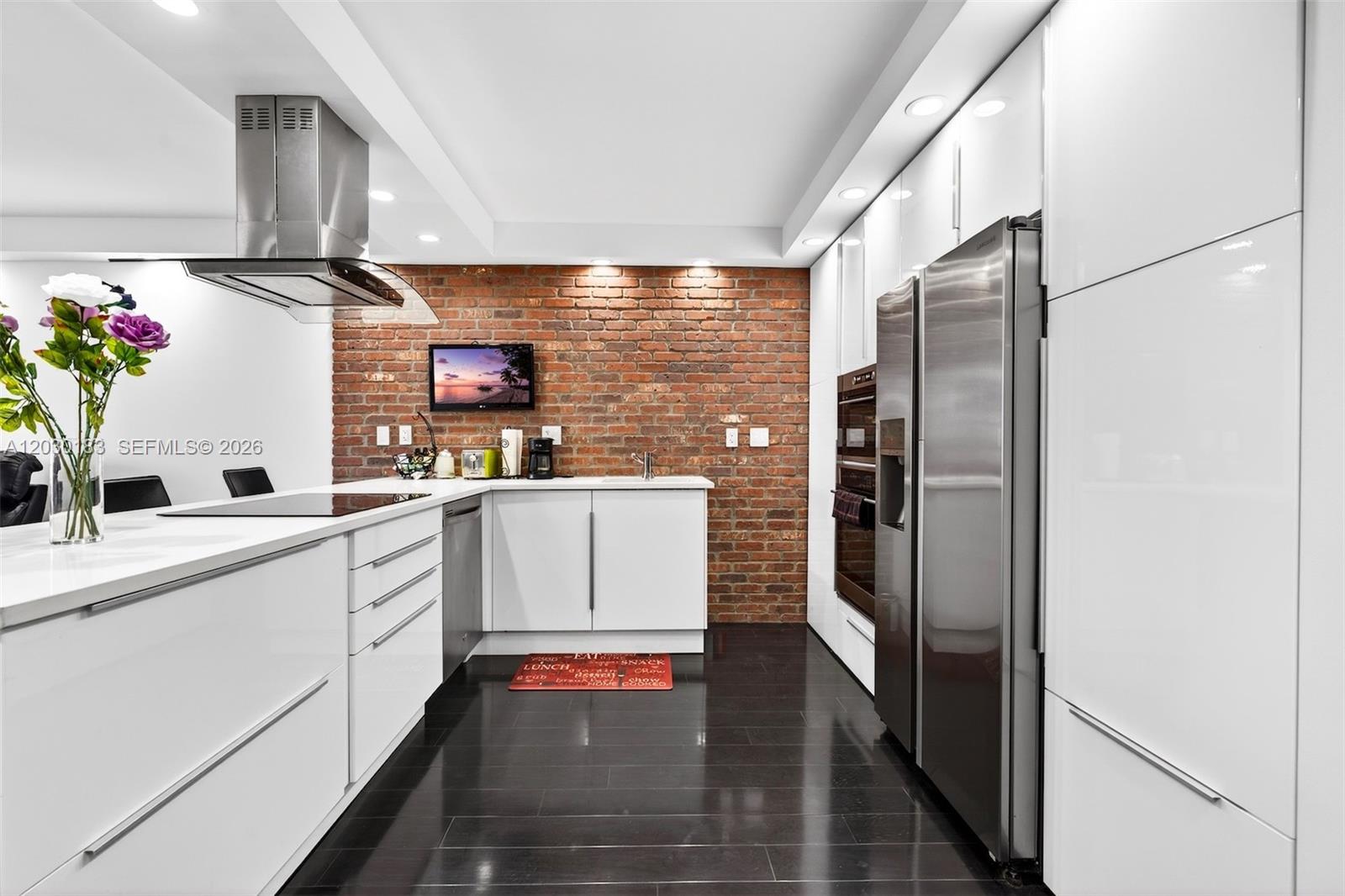 A modern kitchen features white cabinets, stainless steel appliances, and an exposed brick wall — 500 Three Islands Blvd # 201, Hallandale Beach FL 33009, HALLANDALE BEACH, FL