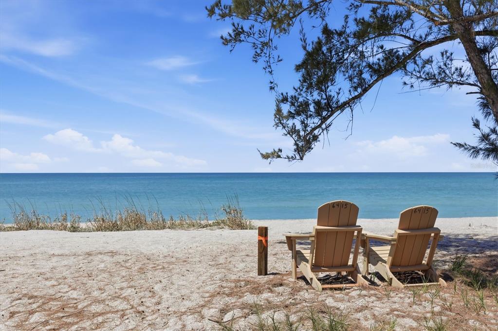 Two wooden Adirondack chairs sit on a sandy beach overlooking the ocean under a tree — 6421 MANASOTA KEY ROAD, ENGLEWOOD, FL