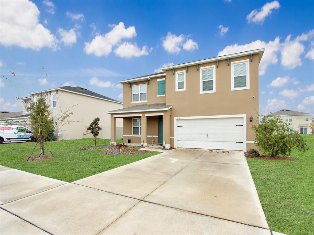A two-story tan house with a white garage door and a concrete driveway — 714 AUBURN GROVE COURT, AUBURNDALE, FL