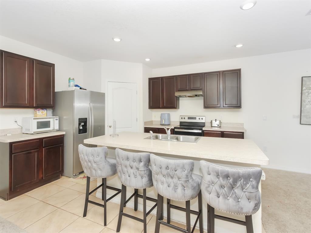 A kitchen features dark wood cabinets, stainless steel appliances, and a central island with seating — 714 AUBURN GROVE COURT, AUBURNDALE, FL