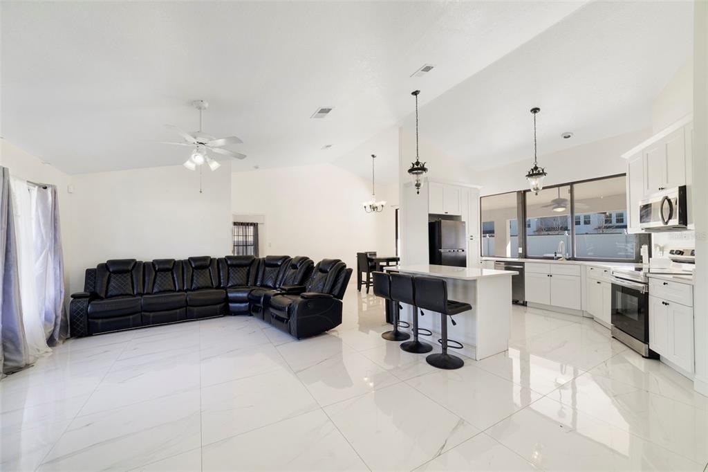 An open-concept living room and kitchen with white tile floors, white cabinets, and black furniture — 247 COMPETITION DRIVE, KISSIMMEE, FL