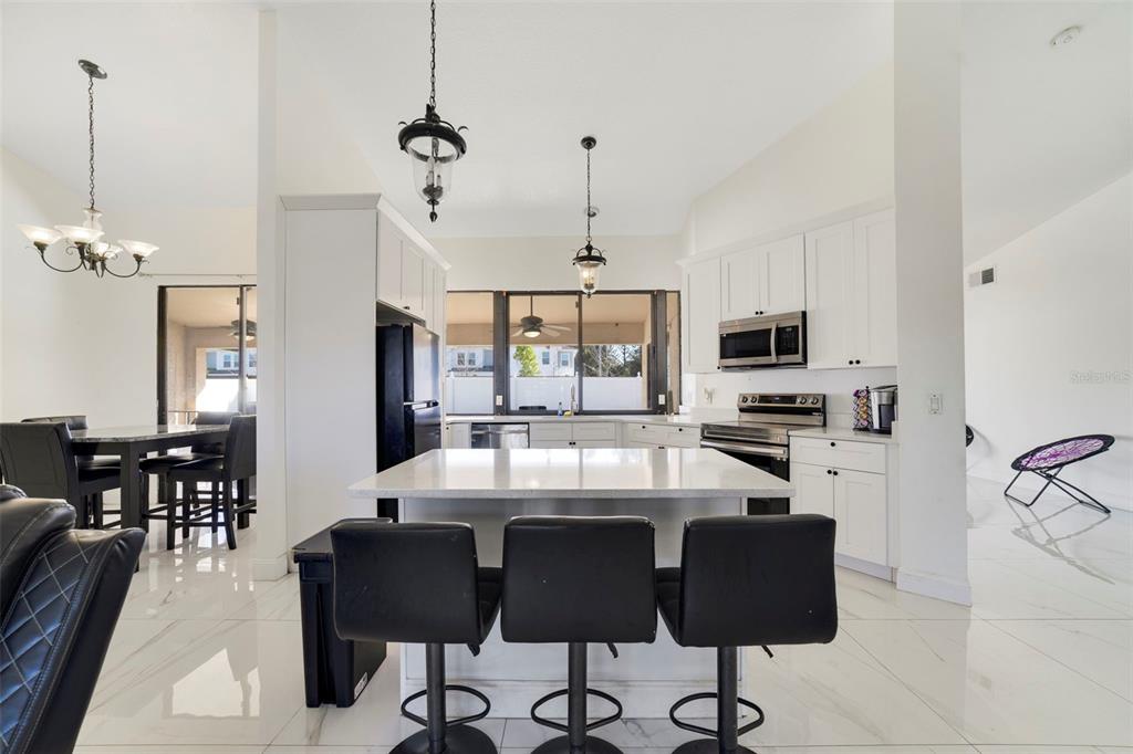 A modern kitchen features white cabinets, a central island with bar stools, and tiled floors — 247 COMPETITION DRIVE, KISSIMMEE, FL