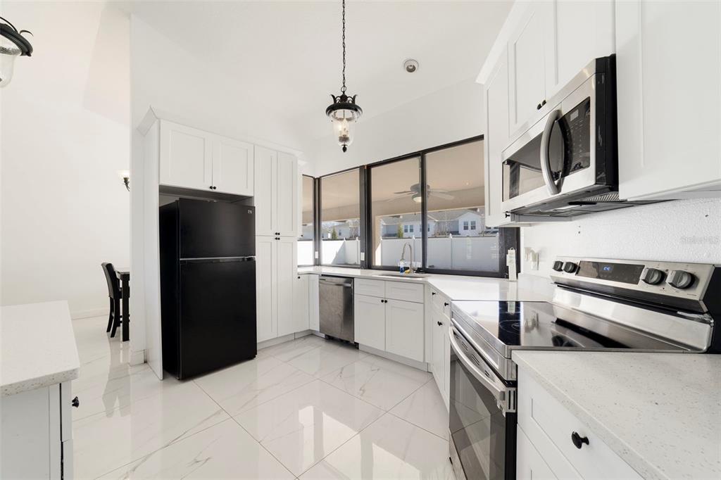 A kitchen with white cabinets, stainless steel appliances, a black refrigerator, and white tile flooring — 247 COMPETITION DRIVE, KISSIMMEE, FL
