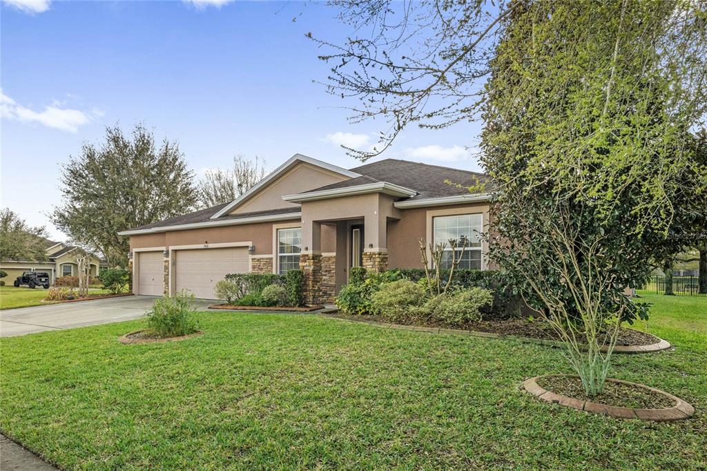 A single-story house with a tan stucco exterior, stone accents, and a three-car garage — 2858 ROLLING HILLS LANE, APOPKA, FL
