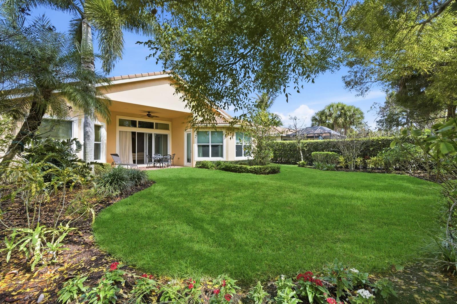 A backyard with a green lawn, landscaping, and a patio attached to a beige house — 160 Carina Drive, Jupiter FL 33478, JUPITER, FL