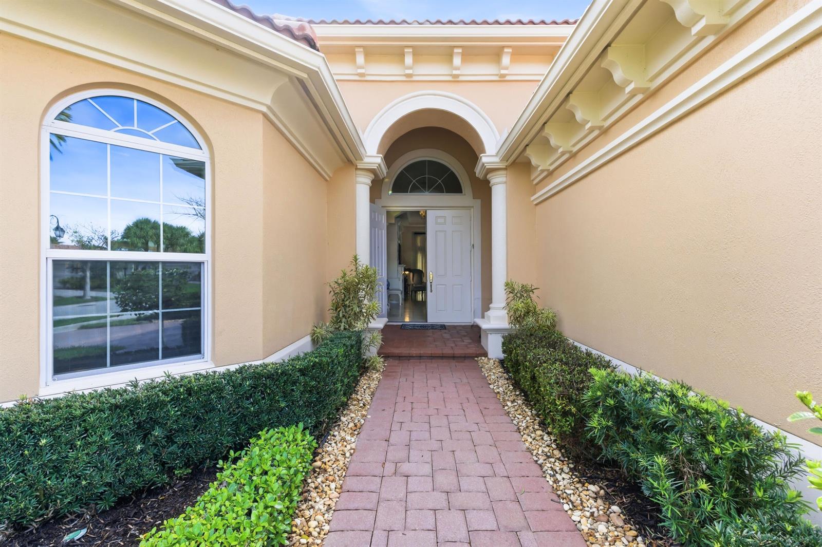 A brick walkway leads to the arched entryway of a tan stucco home — 160 Carina Drive, Jupiter FL 33478, JUPITER, FL