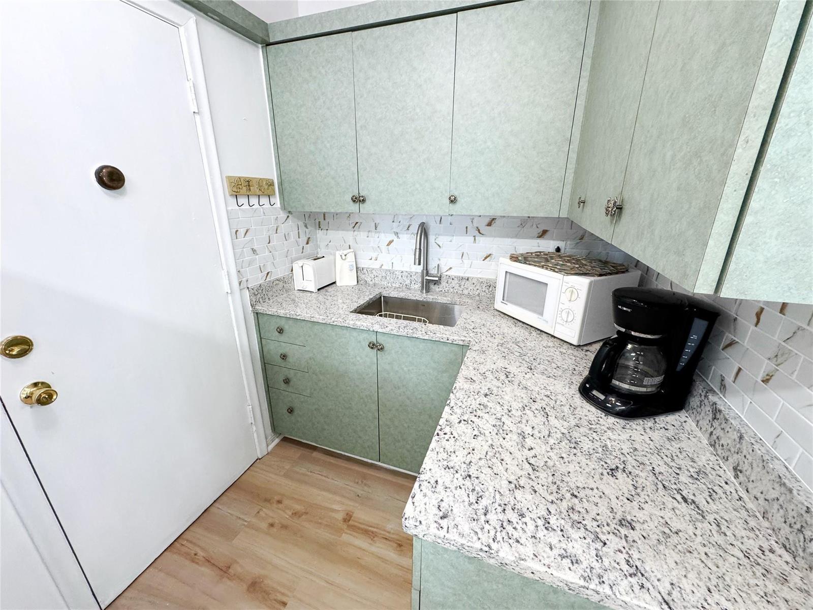 A small kitchen features green cabinets, speckled granite countertops, and a white subway tile backsplash — 310 S Cypress Road # 729, Pompano Beach FL 33060, POMPANO BEACH, FL