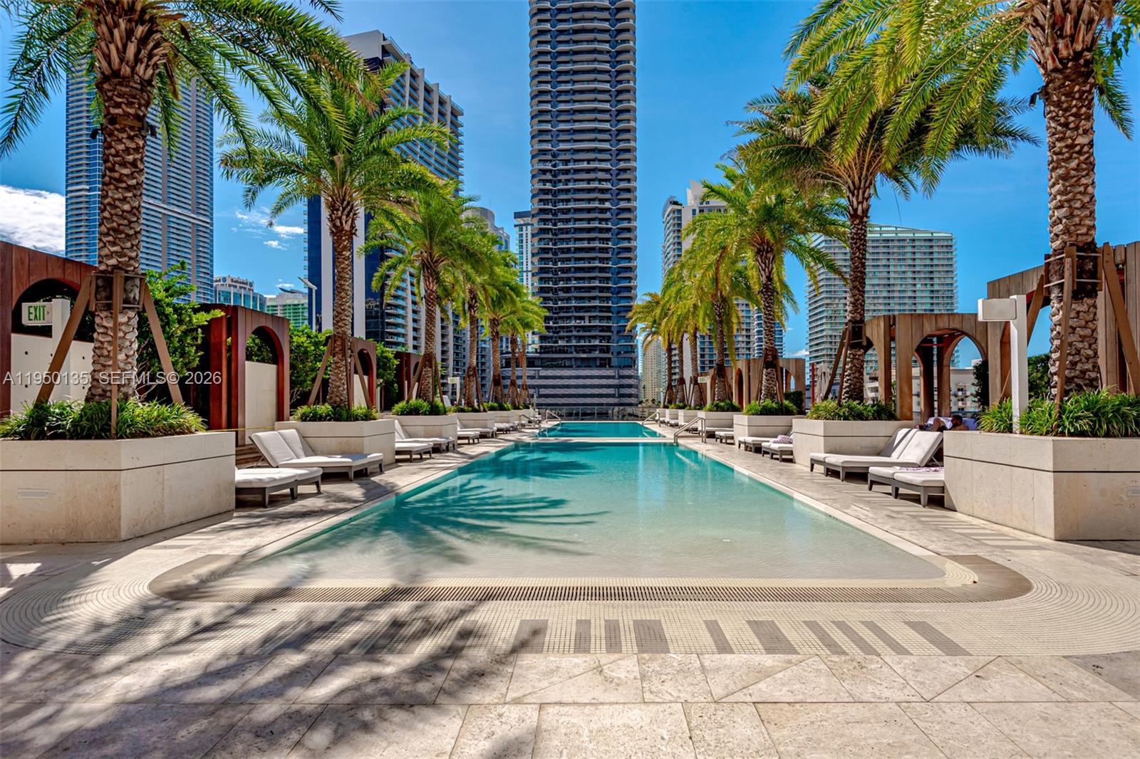 A rectangular swimming pool is surrounded by palm trees, lounge chairs, and modern high-rise buildings — 801 S Miami Ave # 3802, Miami FL 33130, MIAMI, FL