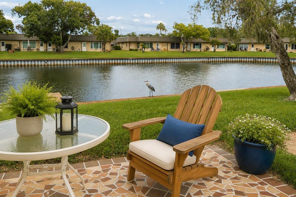 A patio with a glass table, wooden chair, and potted plants overlooks a canal — 4368 SUMMERSUN DRIVE UNIT 4368, NEW PORT RICHEY, FL