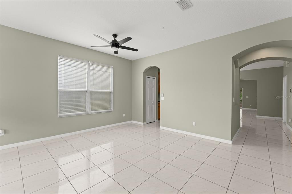An empty room with light-colored tile flooring, beige walls, a ceiling fan, and arched doorways — 14127 SOUTHERN RED MAPLE DRIVE, ORLANDO, FL
