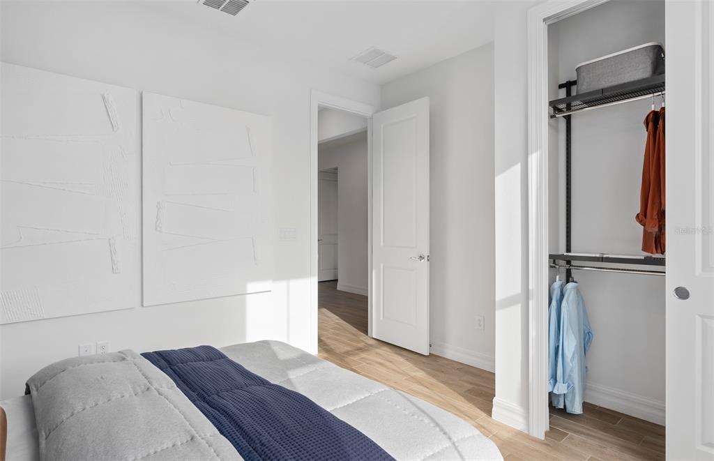 A bedroom features white walls, wood-look flooring, a bed with a blue quilt, and a closet — 2604 SERENITY GARDEN DRIVE, KISSIMMEE, FL