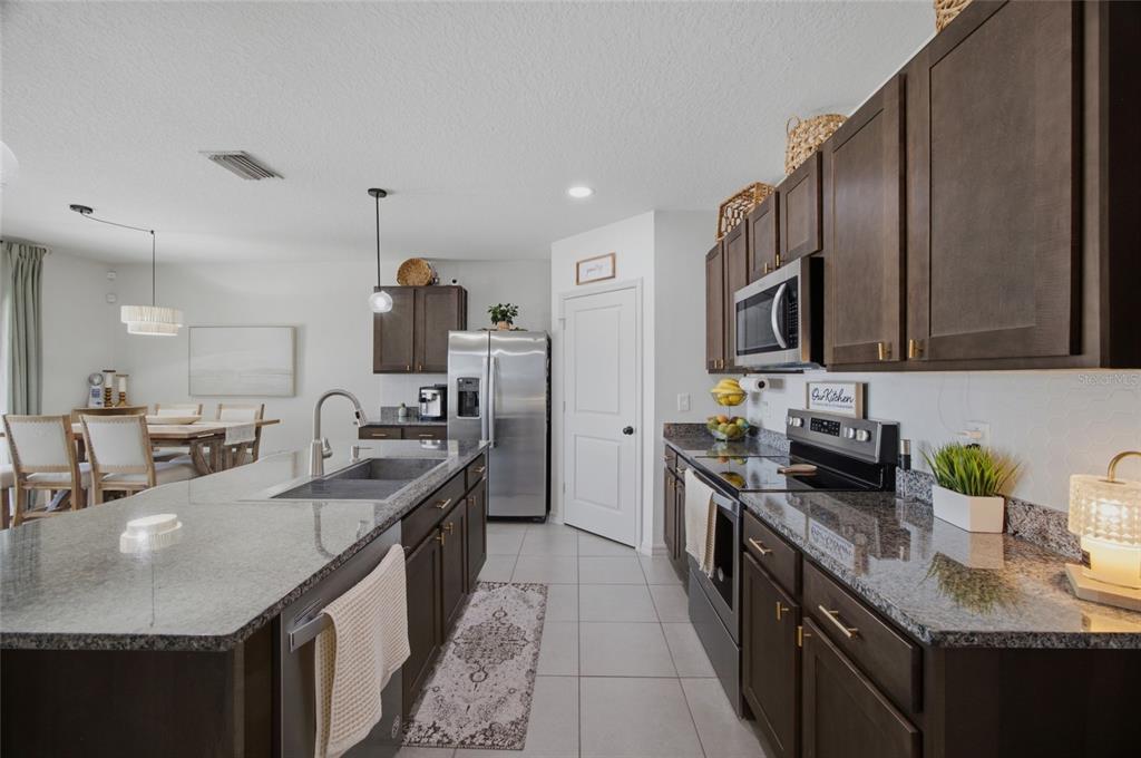 A kitchen features dark wood cabinets, stainless steel appliances, a granite island, and three stools — 2927 LIVING CORAL DRIVE, ODESSA, FL