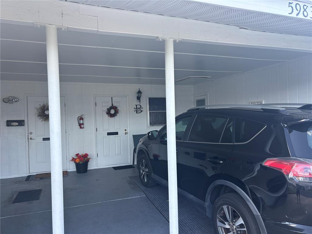 A covered carport area features two white entry doors and a parked black SUV — 5983 CORAL WAY, BRADENTON, FL