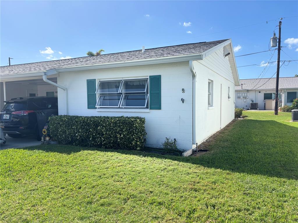 A white single-story house with a carport, teal shutters, and a grassy front yard — 5983 CORAL WAY, BRADENTON, FL