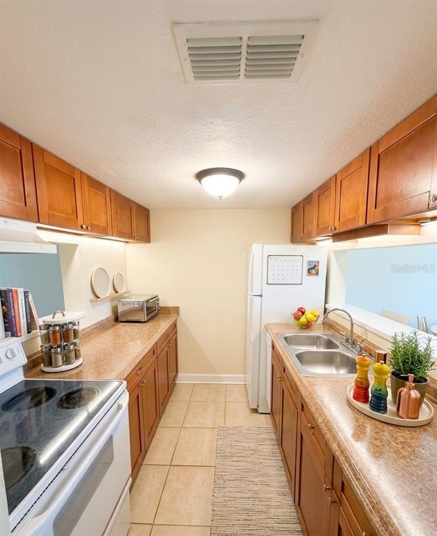 A galley kitchen features wood cabinets, laminate countertops, a white refrigerator, and tile flooring — 7143 E BANK DRIVE UNIT 7143, TAMPA, FL