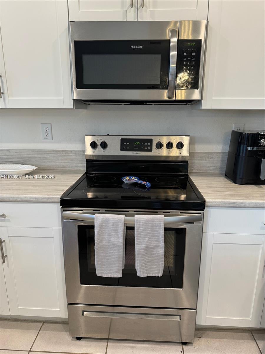 A kitchen features white cabinets, stainless steel appliances, and a glass-top electric range — 21441 NE 3rd Pl, Miami FL 33179, MIAMI, FL