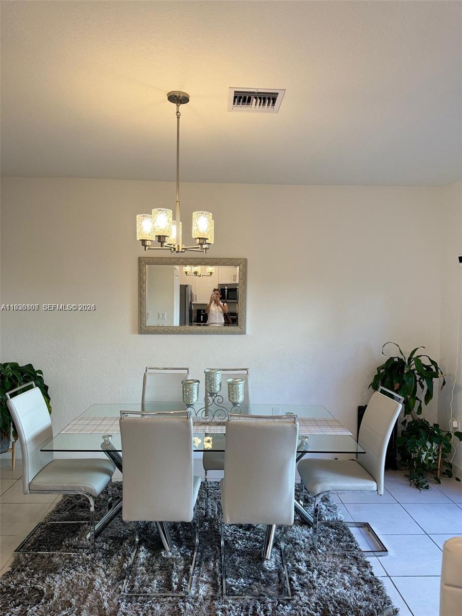 A dining room features a glass-top table, four white chairs, a chandelier, and a mirror — 21441 NE 3rd Pl, Miami FL 33179, MIAMI, FL