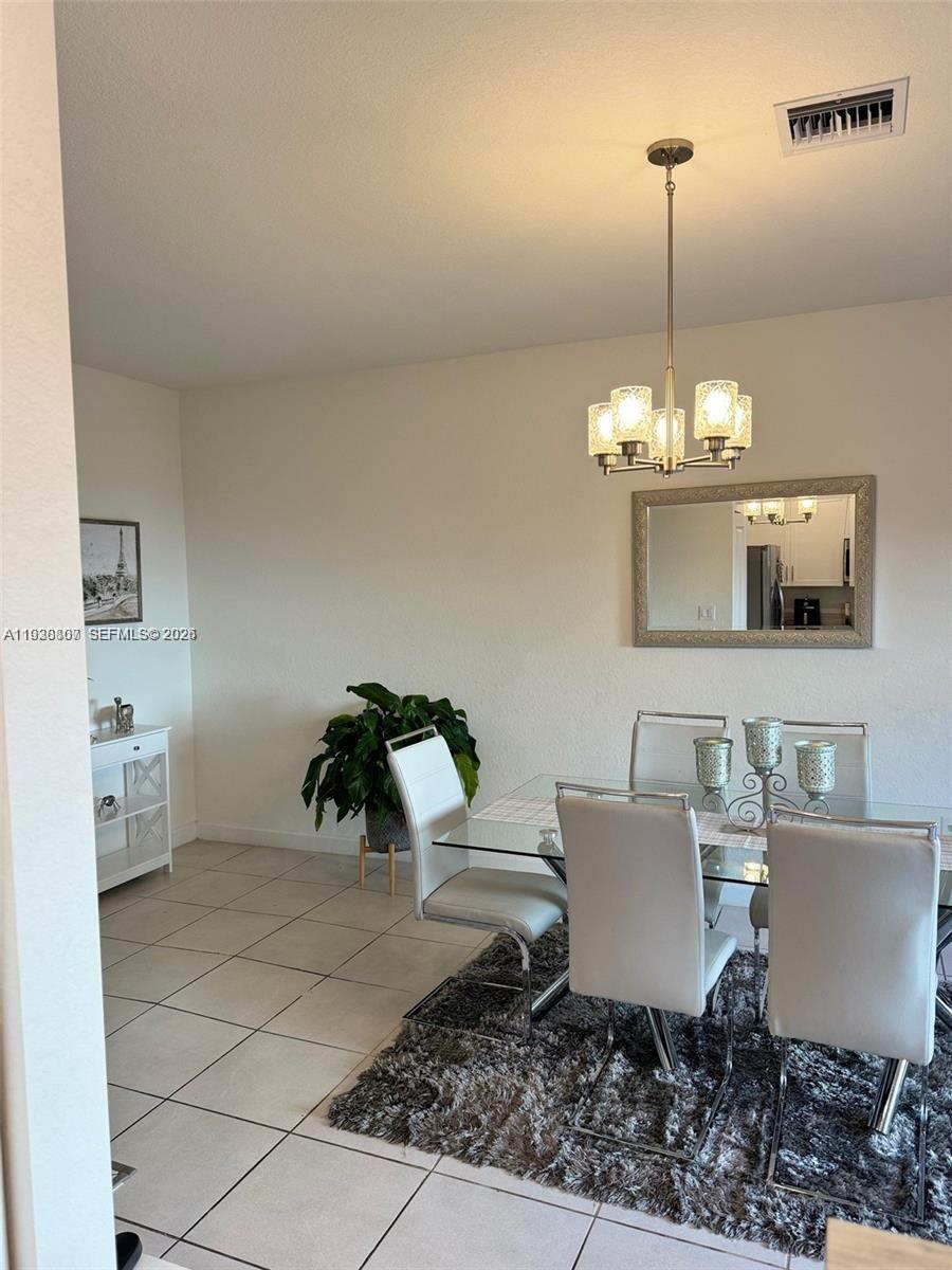 A dining room features a glass table, white chairs, a chandelier, and a wall mirror — 21441 NE 3rd Pl, Miami FL 33179, MIAMI, FL