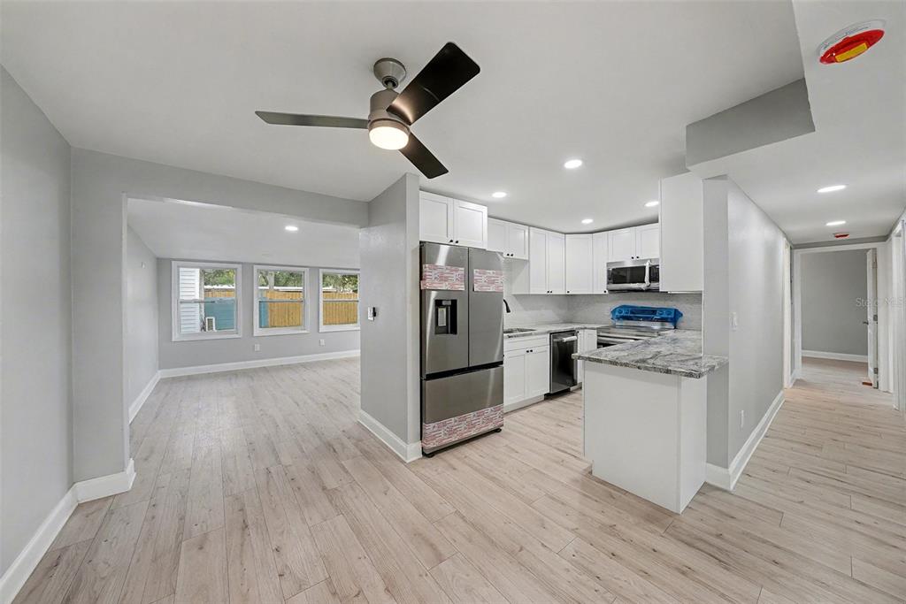 A kitchen with stainless steel appliances and white cabinets opens into a light-filled living area — 2162 BARCELONA DRIVE, CLEARWATER, FL