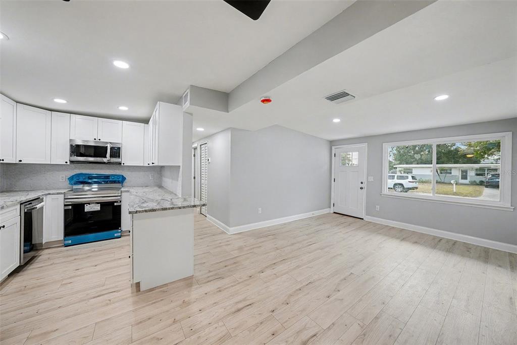 A kitchen with white cabinets and granite countertops opens into a dining area with windows — 2162 BARCELONA DRIVE, CLEARWATER, FL