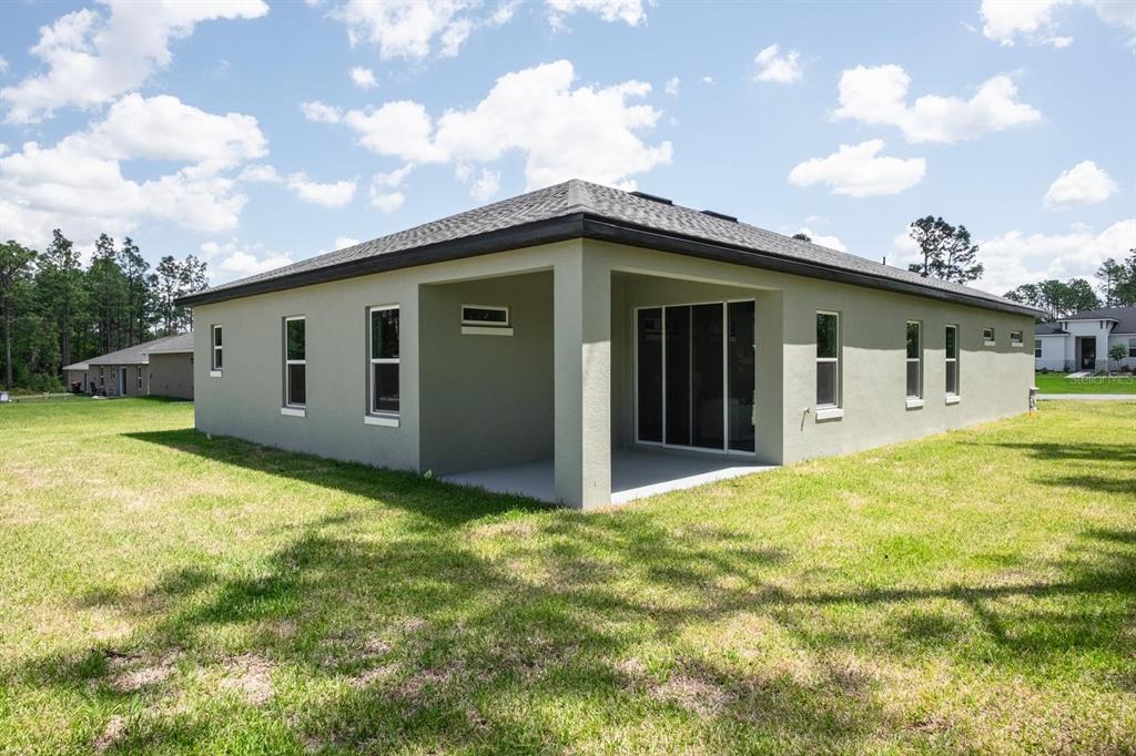 The rear exterior of a single-story house features a covered patio and a grassy yard — 15645 SW 19TH TERRACE, OCALA, FL