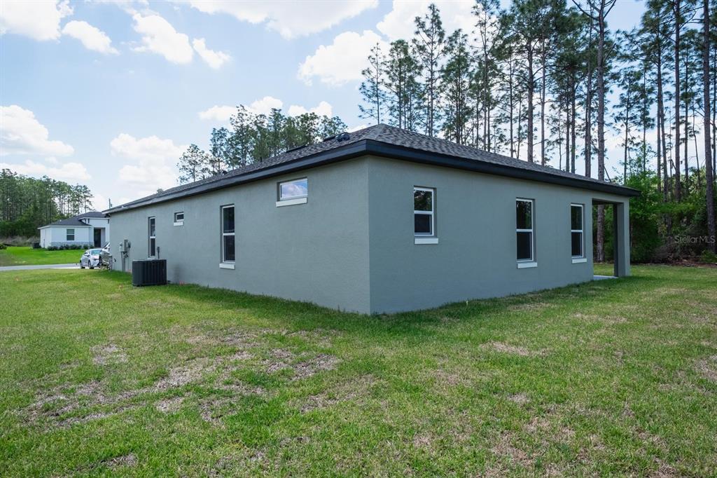 The exterior side and rear view of a gray stucco house with a dark roof — 15645 SW 19TH TERRACE, OCALA, FL