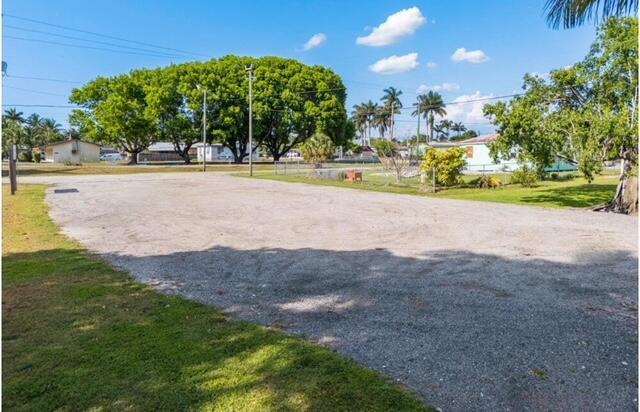 A large, open gravel lot is surrounded by green grass and mature trees — 224 NW G Avenue, Belle Glade FL 33430, BELLE GLADE, FL