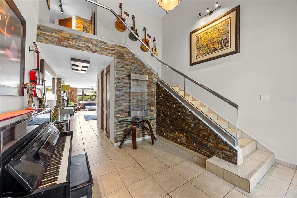 A foyer features a black piano, a stone accent wall, and a staircase with glass railings — 677 PASEO LOS CORALES I, MAR INDICO ST UNIT F-10, DORADO, PR