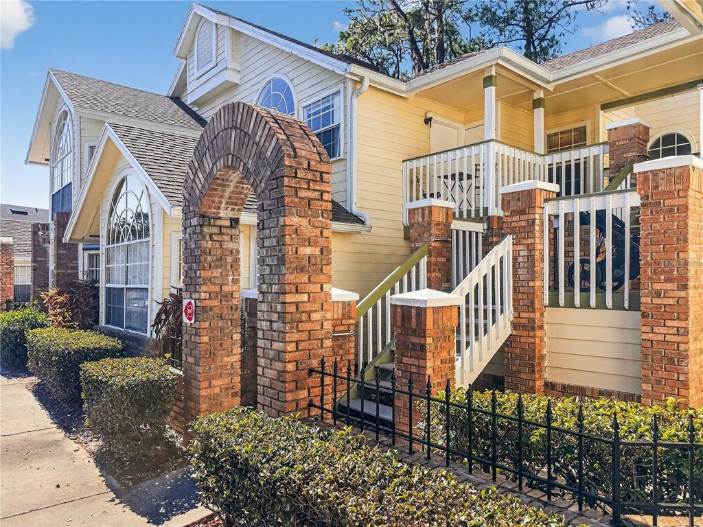 A yellow two-story building features a brick archway, a wooden staircase, and white railings — 5005 LAGUNA BAY CIRCLE UNIT 22, KISSIMMEE, FL