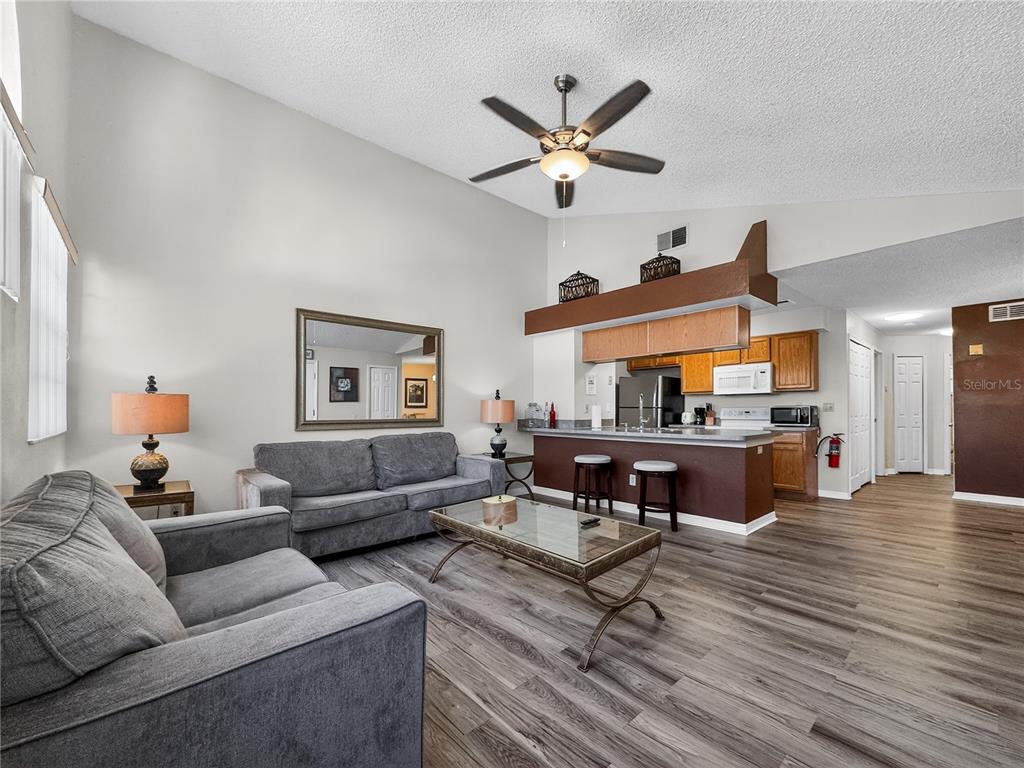 A living room with gray sofas, a glass coffee table, and an open kitchen area — 5005 LAGUNA BAY CIRCLE UNIT 22, KISSIMMEE, FL