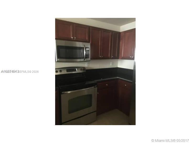 A kitchen features dark wood cabinets, stainless steel appliances, and a black countertop — 11601 NW 89th St # 107, Doral FL 33178, DORAL, FL