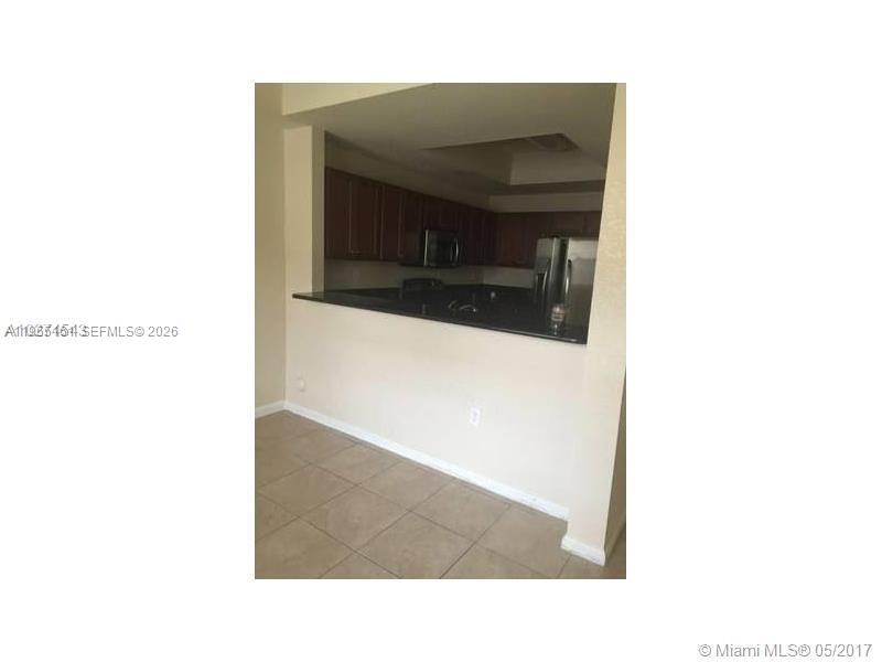 A kitchen with dark wood cabinets and a black countertop overlooks a tiled room — 11601 NW 89th St # 107, Doral FL 33178, DORAL, FL