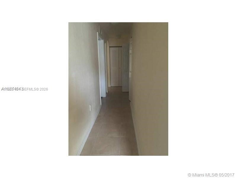 A narrow hallway with beige tile flooring leads to a closed door at the end — 11601 NW 89th St # 107, Doral FL 33178, DORAL, FL