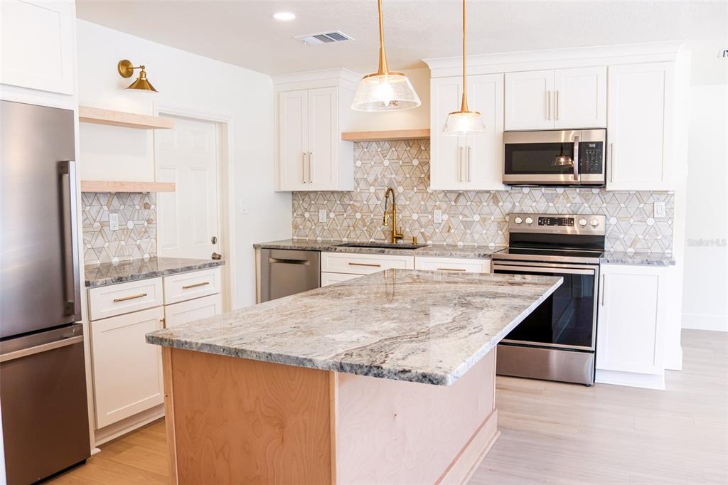 A kitchen features white cabinets, a granite island, stainless steel appliances, and a geometric backsplash — 4211 W BAY VIEW AVENUE, TAMPA, FL