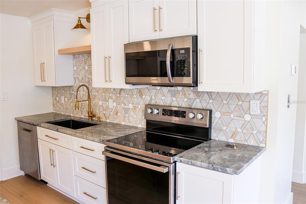 A kitchen features white cabinetry, granite countertops, a geometric tile backsplash, and stainless steel appliances — 4211 W BAY VIEW AVENUE, TAMPA, FL