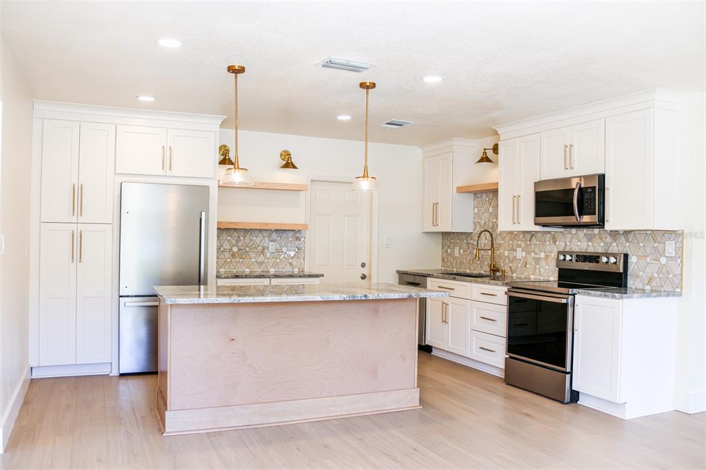 A modern kitchen features white cabinets, stainless steel appliances, a wooden island, and patterned backsplash — 4211 W BAY VIEW AVENUE, TAMPA, FL