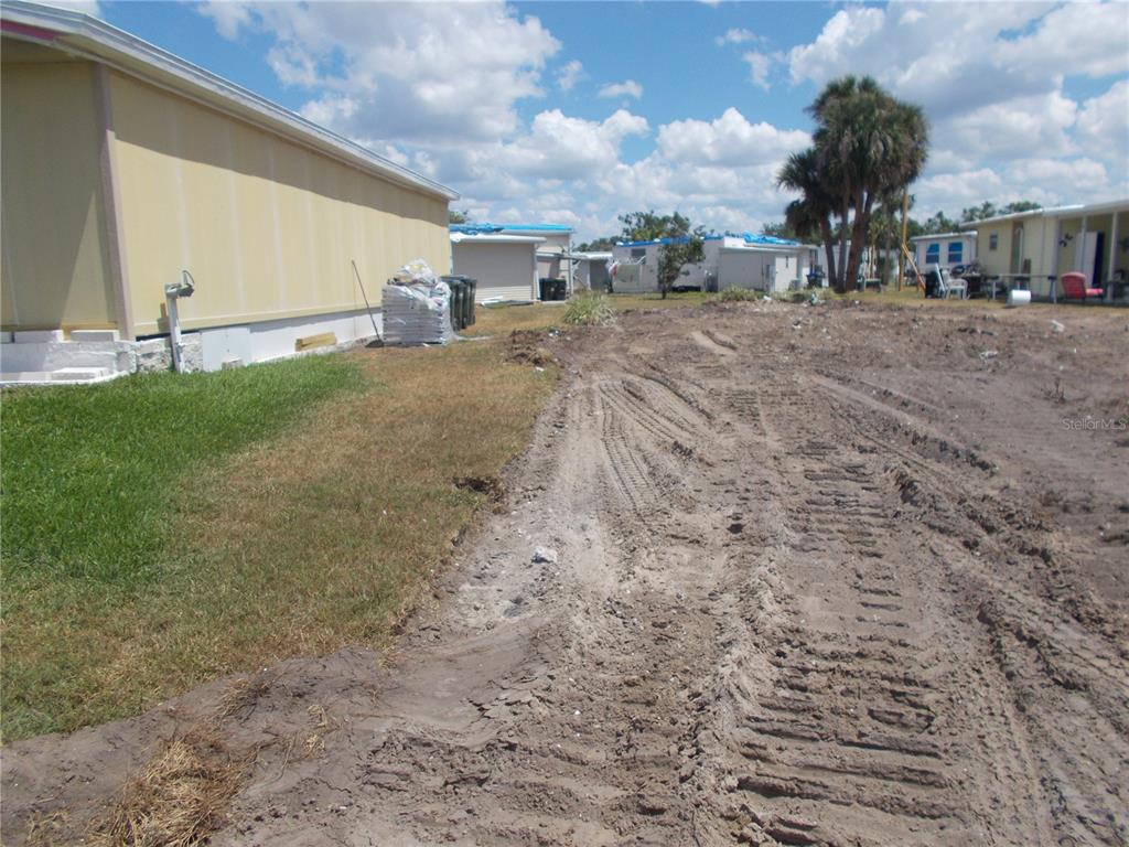 A dirt lot with tire tracks sits beside a yellow mobile home under a cloudy sky — 6706 SAGE LANE, NORTH PORT, FL