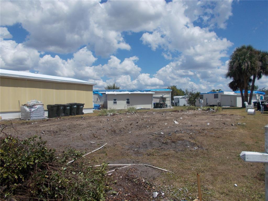 A vacant, cleared lot sits between several manufactured homes under a bright, cloudy sky — 6706 SAGE LANE, NORTH PORT, FL