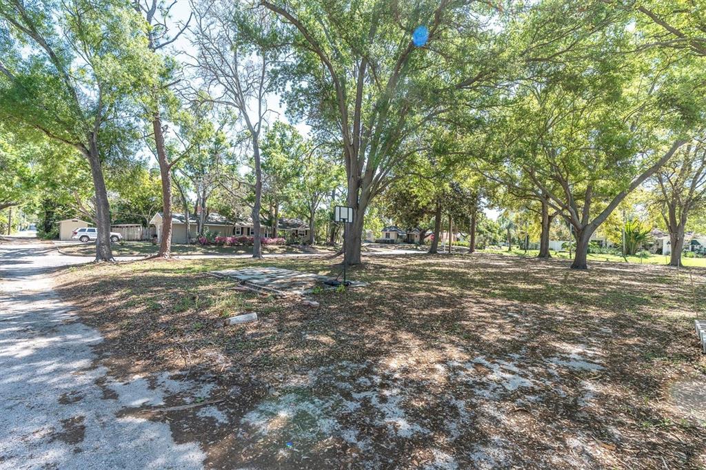 A large, tree-shaded vacant lot features a basketball hoop and a small stone patio area — 6201 11TH AVENUE S, GULFPORT, FL