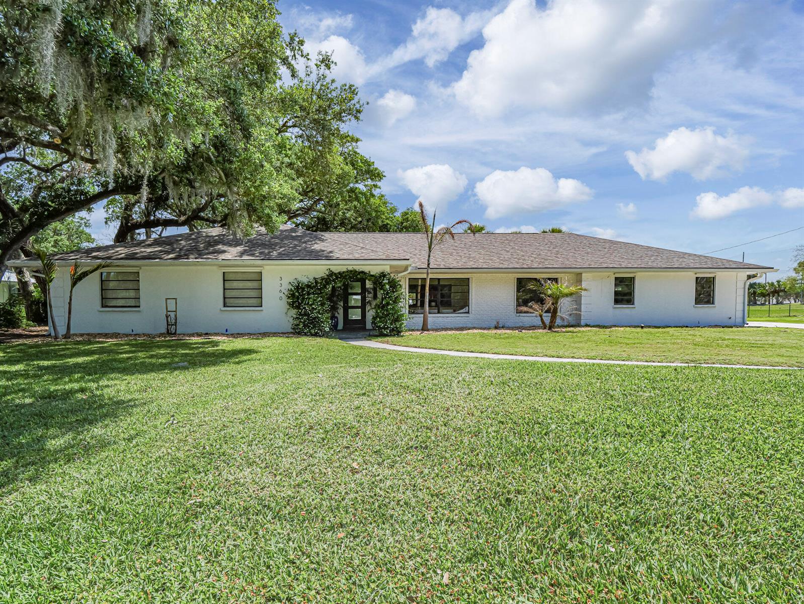 A single-story white brick house with a dark shingled roof and a large front lawn — 3360 Buckinghammock Trail, Vero Beach FL 32960, VERO BEACH, FL