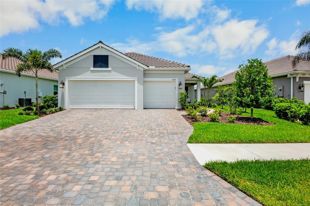 A single-story house with a paved driveway, two garage doors, and a tiled roof — 8091 ANTHIRIUM LOOP, SARASOTA, FL